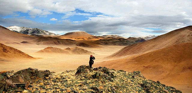 Un voyageur sur un piton rocheux, face à de vastes montagnes ocre